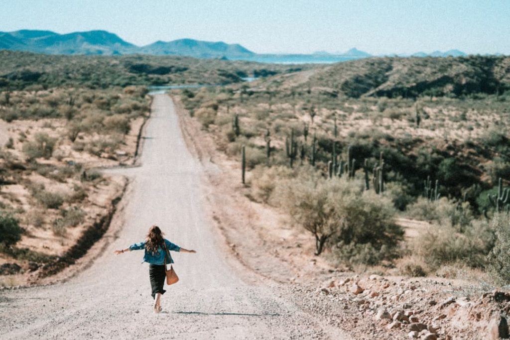 Woman running down a dirt road with cactus on either side and mountains in the distance