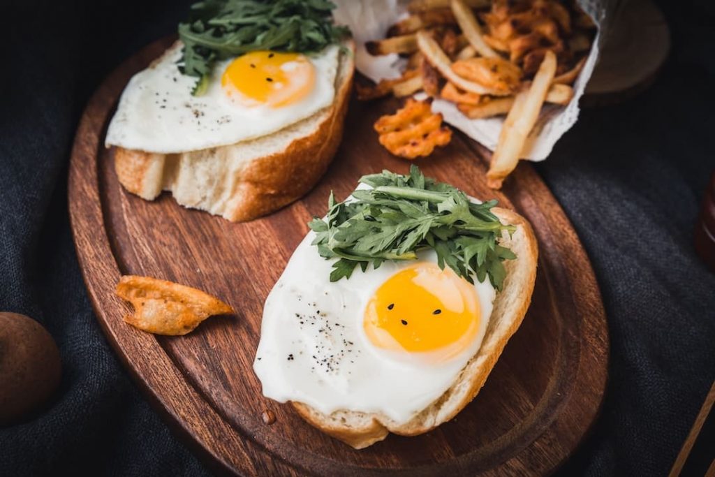 Two pieces of bread topped with a fried egg and french fries in the background