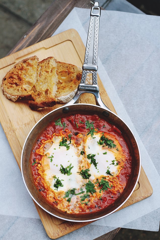 eggs cook in bright read tomatoes served with some slices of bread