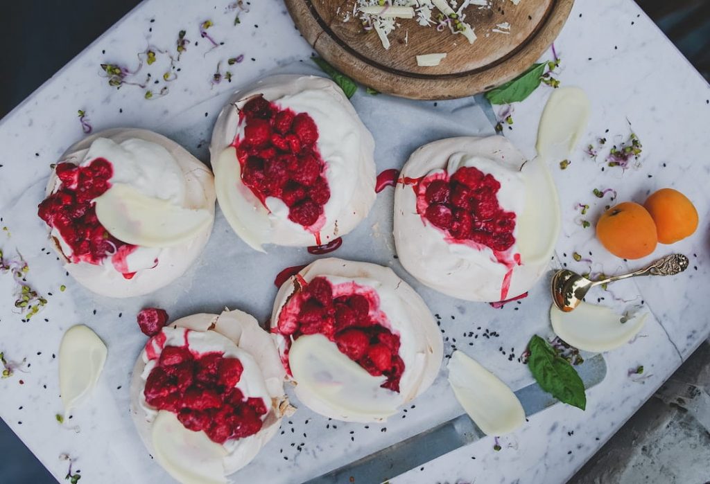 Pavlova topped with whipped cream and raspberries
