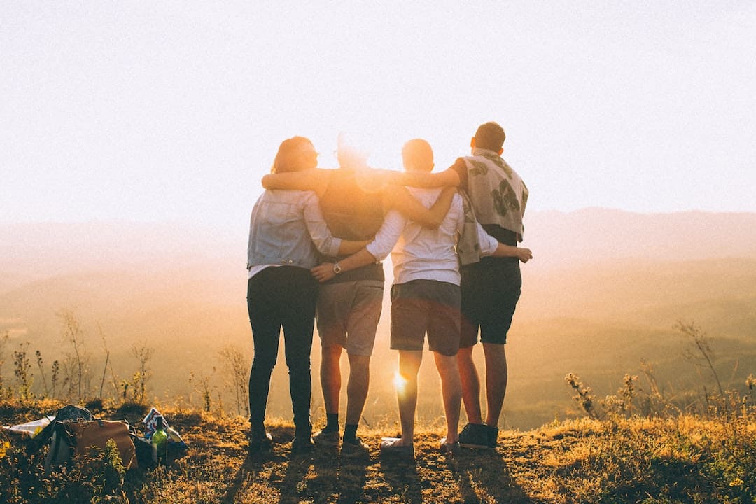 Group of friends with their arms around eachother and a sunset in front on them