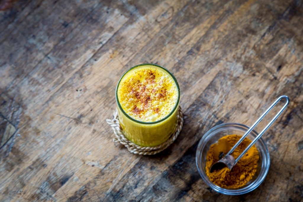 A glass cup filled with a turmeric latte and a small bowl with turmeric powder
