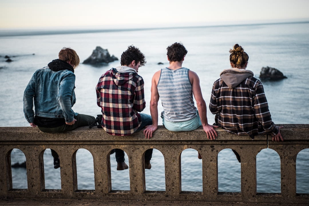 Four people sitting on a railing overlooking the sea