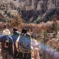 Three hikers walking through a canyon wearing backpacks