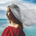 a woman in a red dress and veil beside the sea