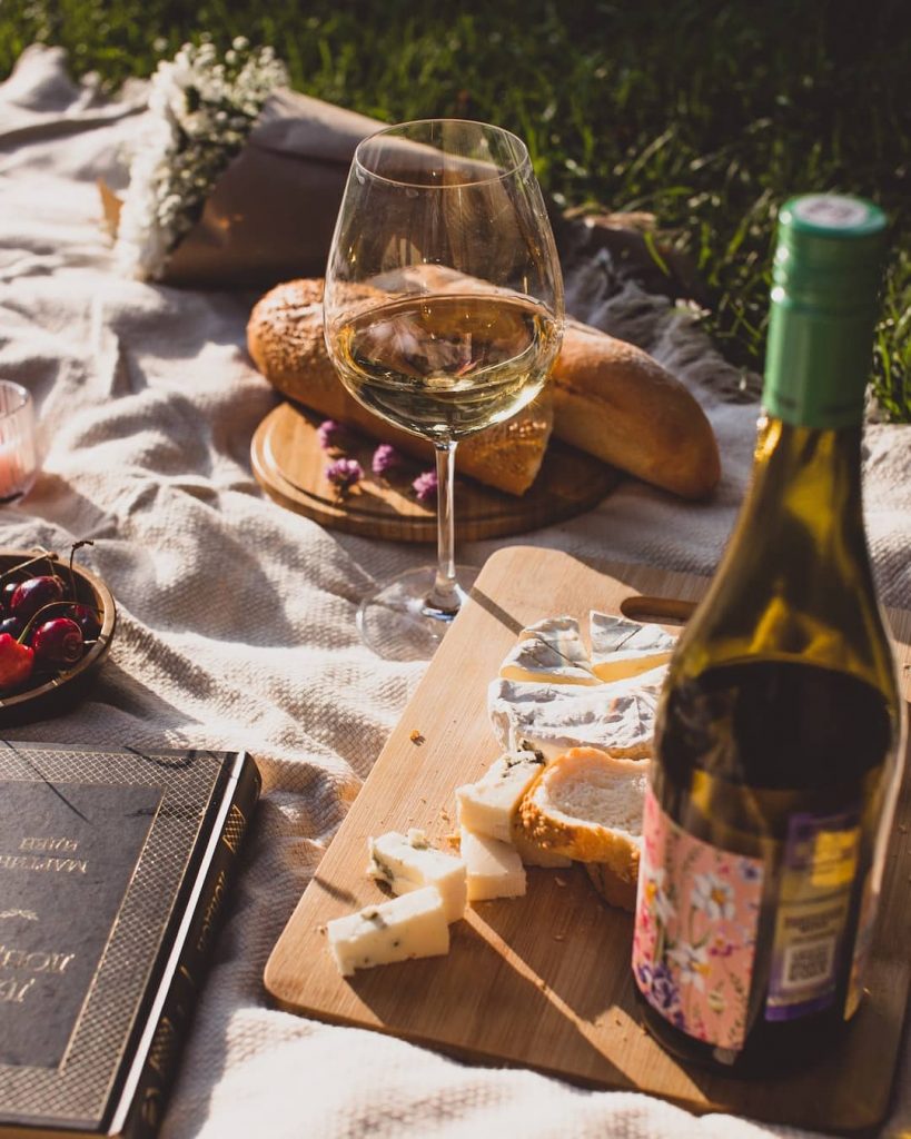 Picnic spread with wine bottle, cheese platter, and a baguette
