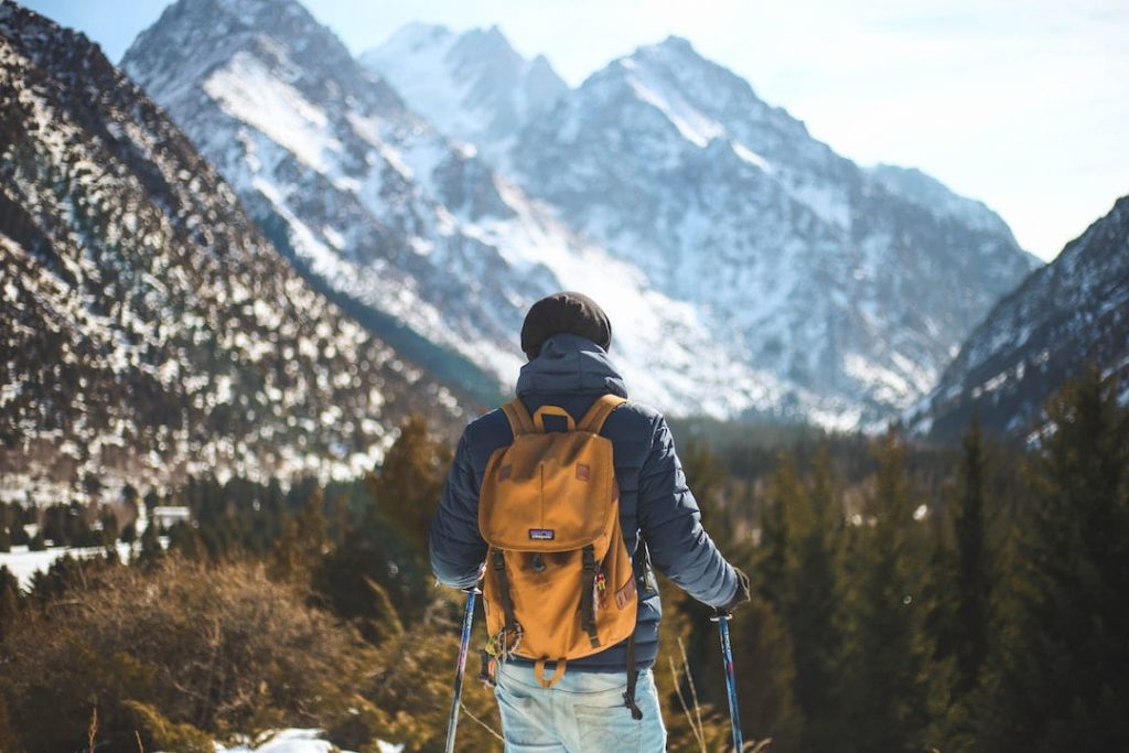Man wearing a yellow backpack and standing in front of mountain peaks