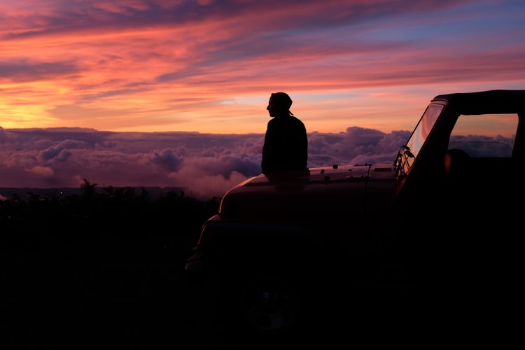 a man sitting on his bonnet overlooking a pink sunset