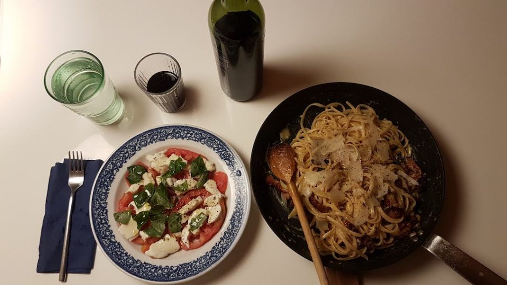 Tomato mozarella salad, a pan filled with pasta, and a bottle of wine