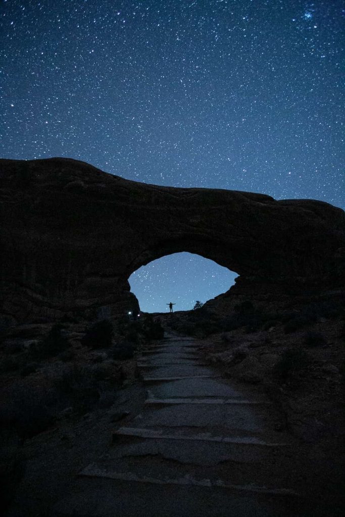 Person standing under starlit sky in Arches National Park, Utah