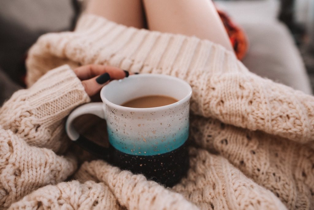 Person wearing a chunky sweater with a cup of tea in their lap