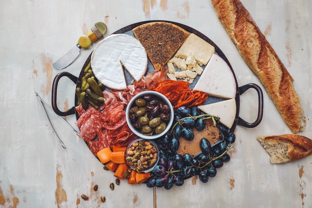 Cheese board with meat, olives, grapes, and a baguette