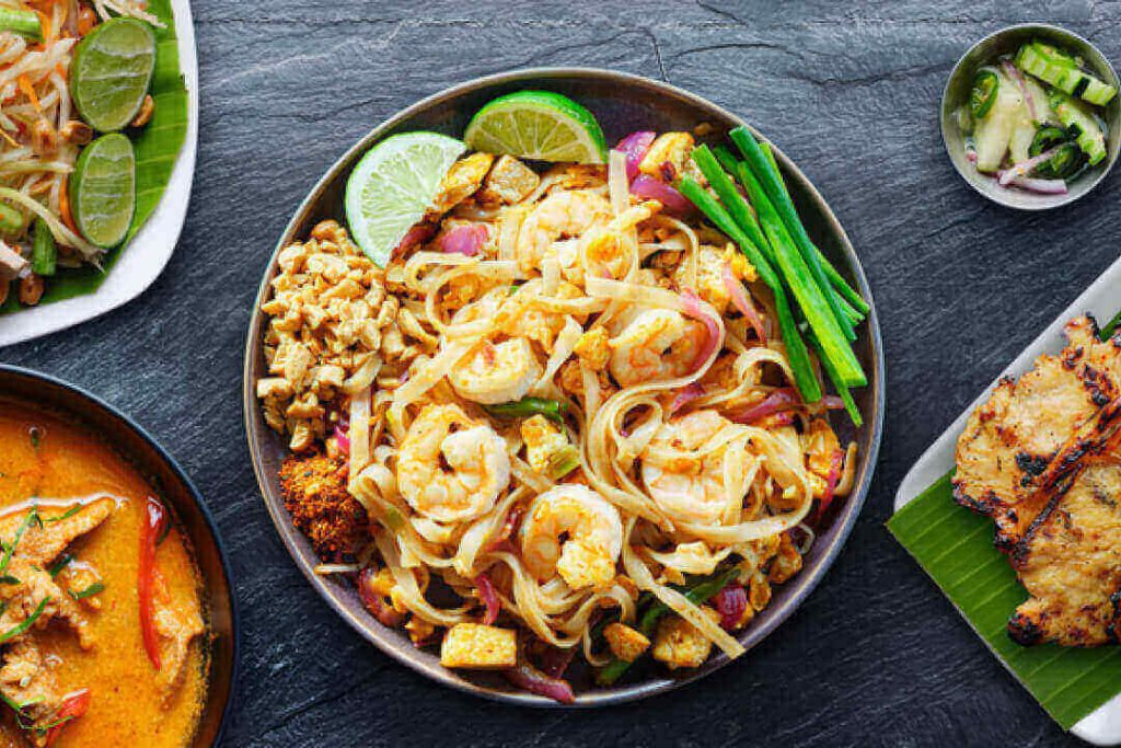 An assortment of Thai food with shrimp pad Thai, curry, and a couple of other dishes.
