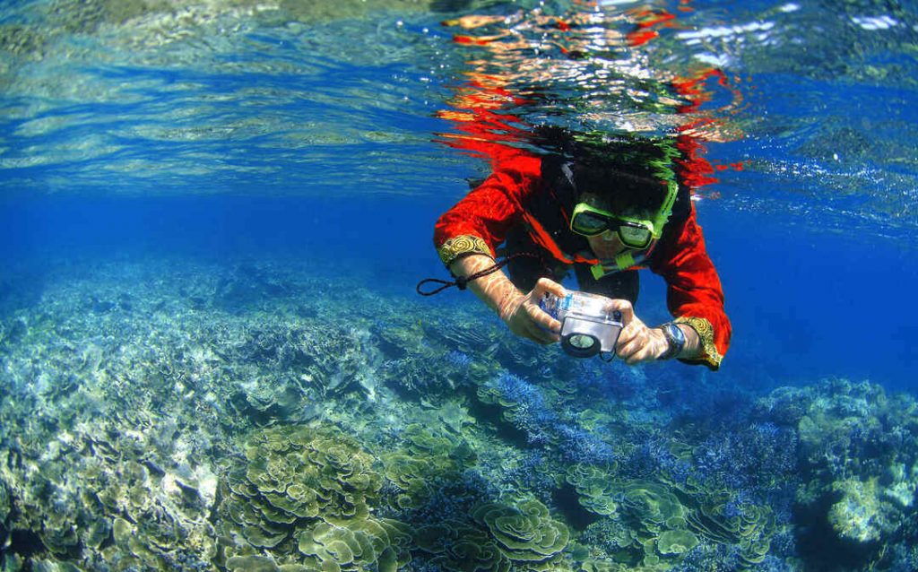 A person snorkels with a camera in the crystal clear water of the Mu Koh Surin National Park, Thailand.