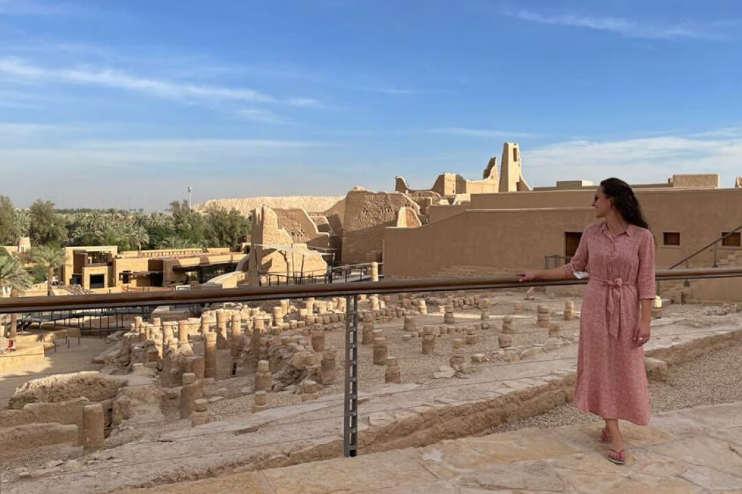 The speck of a woman standing near an ancient site in Saudi Arabia
