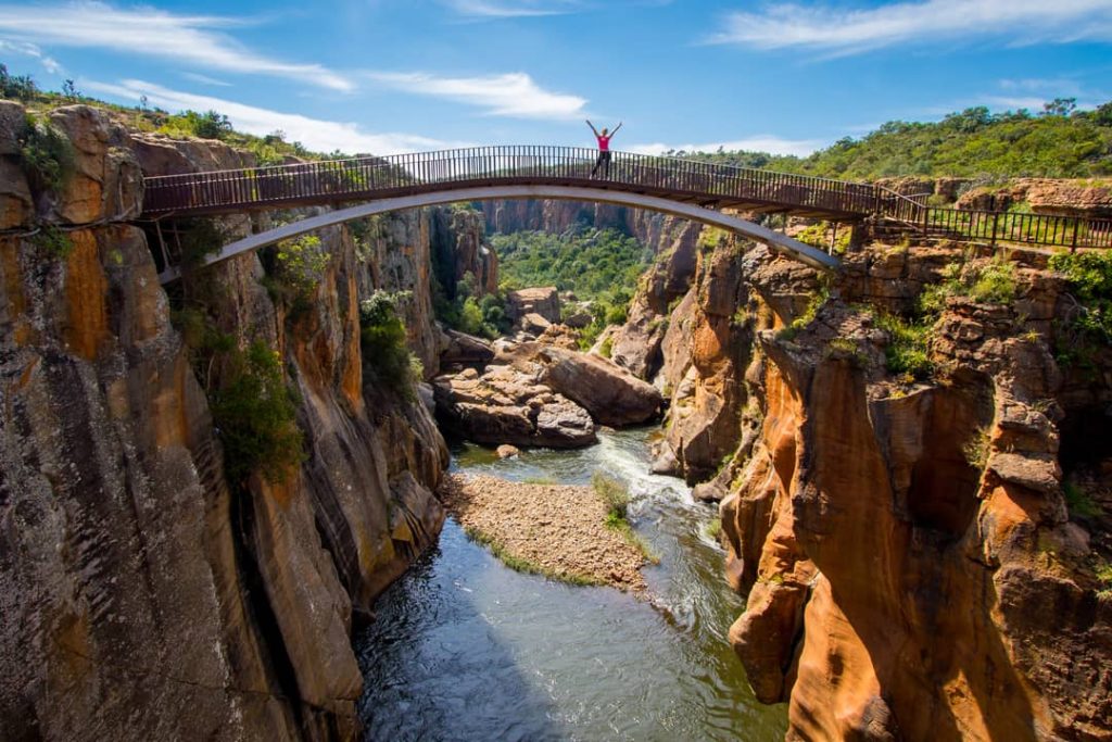 A woman embraces wellness by connecting with nature on the bridge over Bourke's Luck Potholes geological formation in the Blyde River Canyon, South Africa.