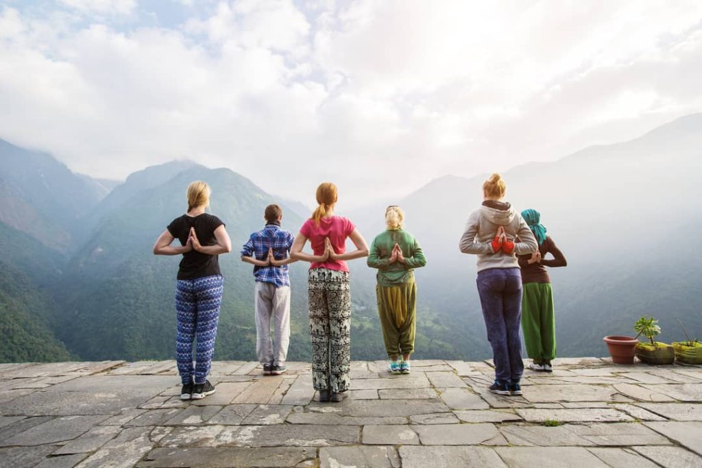A group of six women are increasing their well-being by doing standing yoga exercises with their backs to us.