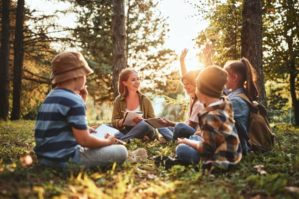School kids learn about ecology and nature conservation with their teacher while sitting together in the forest.