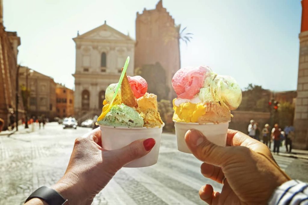 A couple holds up their delicious, colorful gelato for a picture and uses the lovely square in Rome, Italy as the background.